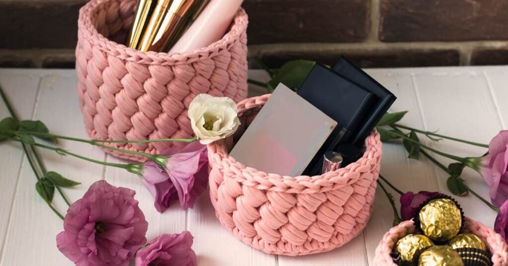 Organizadores de crochet en color rosa, tejidos a mano con trapillo, utilizados para almacenar maquillaje y accesorios.